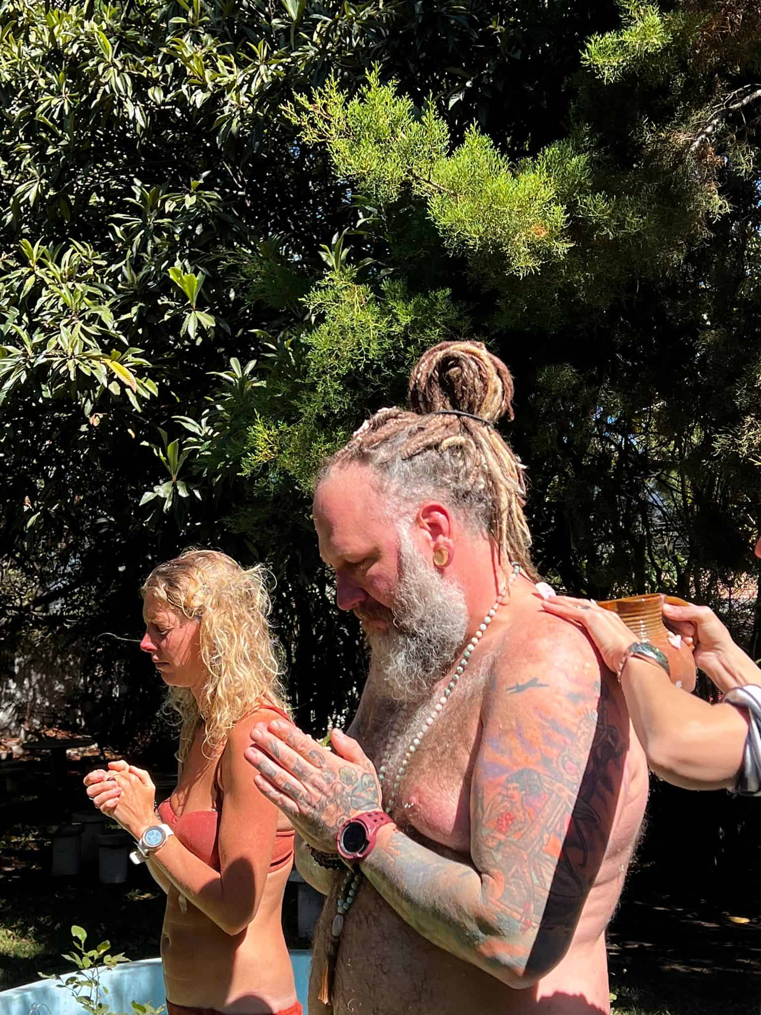 Shirtless man and woman in a bathing suit receiving flower ceremony after plant retreat