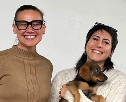 Two women, director of Retreat smile at camara while one holds a puppy